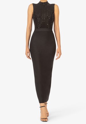 Robe noire sans manches avec un corsage ajusté orné de détails texturés à clous et une jupe longue et étroite. Comprend un décolleté subtil et une accentuation à la taille.