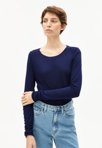 Marineblauwe longsleeve shirt met ronde hals, gemaakt van gladde stof, gecombineerd met hoogtaille lichtblauwe jeans met een knoopsluiting.