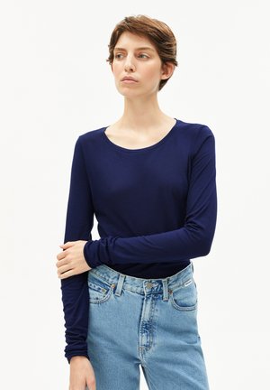 Marineblaue Langarmbluse mit Rundhalsausschnitt, aus glattem Stoff, kombiniert mit hochtaillierten hellblauen Jeans mit Knopfverschluss.