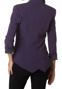 Femme portant un blazer violet ajusté aux manches retroussées et un pantalon noir, vue de dos sur un fond blanc.