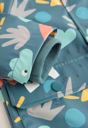 Vandtæt jakke med teal bundfarve og farverige geometriske mønstre, elastiske manchetter og trykknap foran.