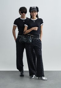 Svarta tajta t-shirts med vita detaljer, svarta mönstrade byxor och en svart handväska. Accessoarerna inkluderar solglasögon och en keps med päls.