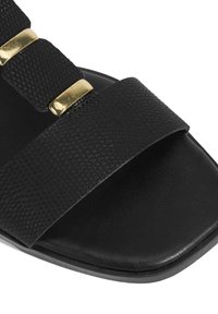 Black sandal featuring two textured straps, one with a woven pattern and gold-toned accents. Smooth sole with a rounded shape.