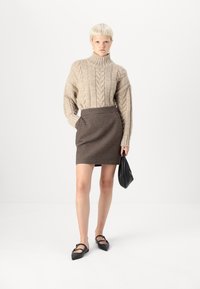 Jersey de punto beige con cuello alto, combinado con una falda lápiz marrón a cuadros. La modelo sostiene un bolso negro. Bailarinas negras con tiras.