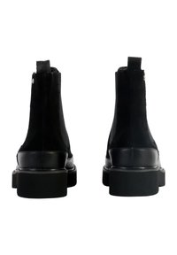 Bottines en daim noir avec une semelle en cuir noir lisse, dotées d'un bout arrondi et d'un léger talon, avec des poignées à l'arrière.
