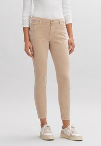 Pantaloni in corduroy beige con una vestibilità slim, dotati di tasche frontali, chiusura a bottone e un tessuto leggermente testurizzato. Abbinati a sneakers bianche.