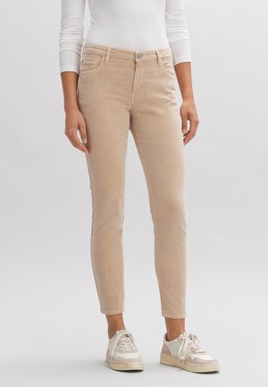 Pantalons en velours côtelé beige avec une coupe slim, dotés de poches avant, d'une fermeture à bouton et d'un tissu texturé subtil. Assortis à des baskets blanches.