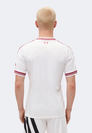 Personne aux cheveux blonds courts portant un maillot de sport blanc avec des rayures rouges sur les manches et le col, vue de dos.