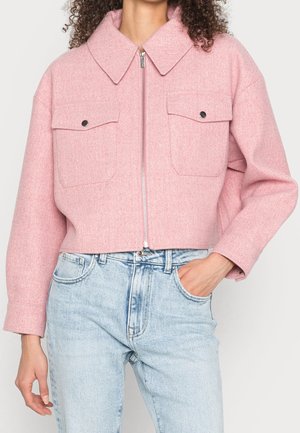 Kvinde iført en cropped pink uldjakke med frontlynlås og klaplommer, kombineret med lyseblå højttaljede jeans.