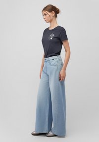 Navy cotton t-shirt with a cat graphic, paired with light blue wide-leg jeans. The jeans feature a high waist and subtle stitching details.