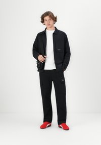 Chaqueta negra con bolsillo en el pecho, camiseta blanca, pantalones cargo negros y zapatillas rojas. Diseño simplista, textura suave, estilo casual.