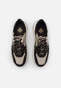 Černé a zlaté tenisky s horní částí z síťoviny a kůže. Mají zaoblenou špičku, silné tkaničky, polstrovaný jazyk a texturované detaily po celém povrchu.