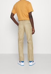 Beige kordbyxor med rak passform, som har två bakfickor och en diskret logotypapplikation på höger ficka.