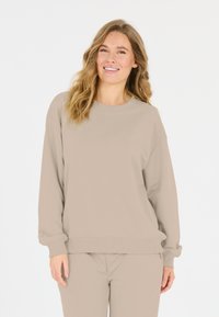 Beige collegepaita pehmeästä kankaasta, jossa rento malli, pudotetut olkapäät ja ribbaatut hihansuut. Yhdistetty vastaaviin bežejogger-housuihin.