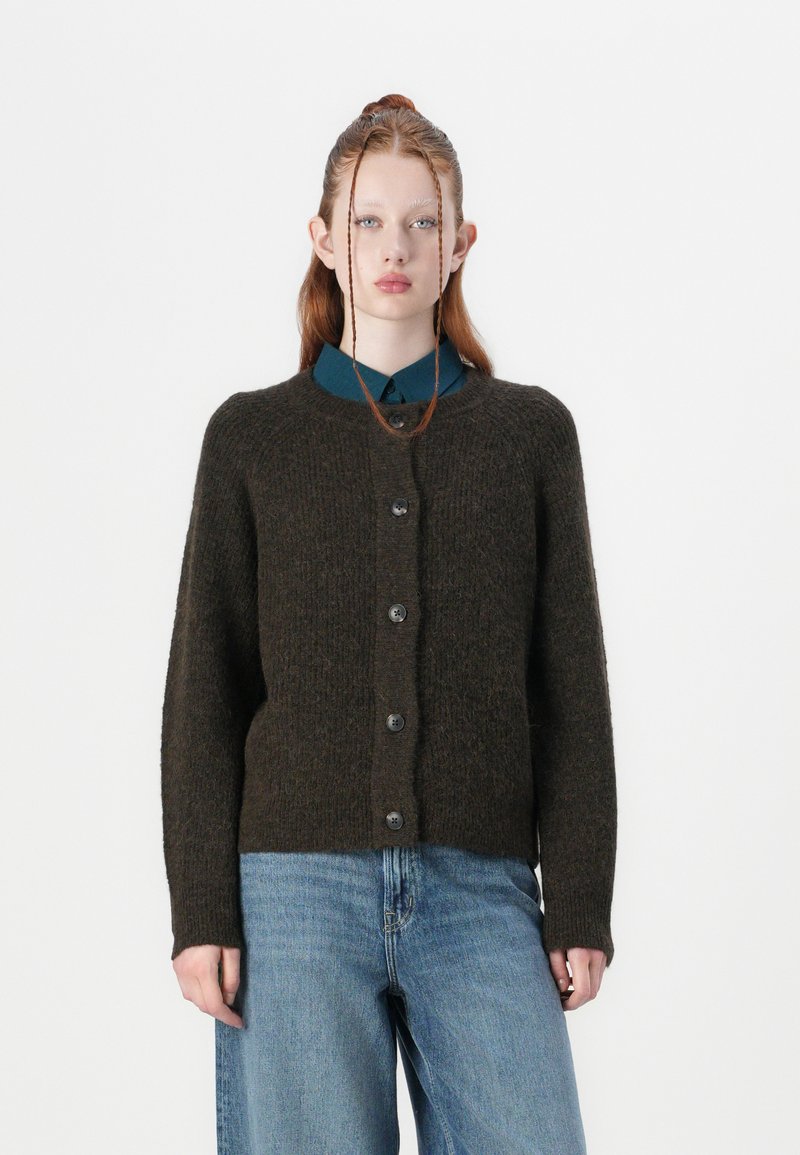 Dark green knitted cardigan with a round neckline and button closure. Features a textured finish and ribbed cuffs. Worn over a blue shirt.