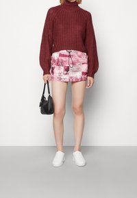 Bordeaux gebreide trui met ballonmouwen, gecombineerd met een roze gemusterde mini-jurk met een trekkoord en grafische elementen. Witte sneakers en een zwarte handtas.