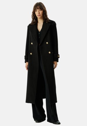 Manteau en laine noir à double boutonnage avec boutons dorés, revers crantés et manches longues avec détail aux poignets, descendant jusqu'au mollet.