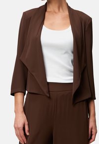 Ruskea, kevyt, avoin edestä oleva takki, jossa on 3/4-hihat ja laskeutuva muotoilu, yhdistettynä valkoiseen istuvaan toppiin. Sileä pinta, ei näkyviä kuvioita.