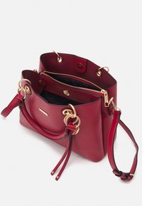 Sac à main en cuir rouge avec un design structuré, quincaillerie dorée, double poignées et une bandoulière réglable. L'intérieur comprend une poche zippée.