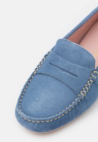 Sinine sametist loafers, millel on õmmeldud muster, sujuva pealse, kerge kanna ja roosa sisetallaga.
