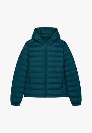 Femme portant une doudoune turquoise à capuche, un jean bleu clair retroussé et des baskets blanches, debout et regardant par-dessus son épaule.