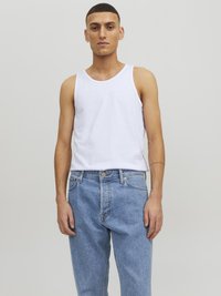 Débardeur en coton blanc avec un col rond, associé à un jean en denim bleu clair. Le tissu semble doux ; la coupe est ample et décontractée.