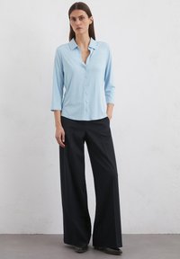 Light blue button-up shirt with a collar and three-quarter sleeves, paired with black wide-leg trousers in a smooth fabric.