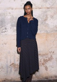 Granatowy sweter na drutach z wzorem warkocza, zapinany na guziki, z długimi rękawami; zestawiony z asymetryczną spódnicą w paski w kolorach ciemnoniebieskim i brązowym.