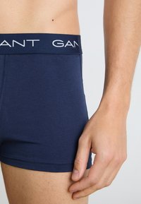 Mann trägt marineblaue Boxershorts mit sichtbarem elastischem Bund, der mit dem Text "GANT." gebrandet ist