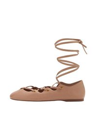 Bailarina con cordones en suave material beige, que presenta un diseño recortado, ojales dorados y una correa espiral en el tobillo para un ajuste seguro.