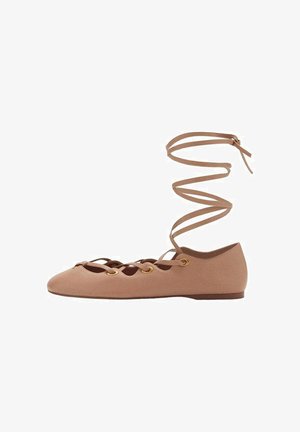 Bailarina con cordones en suave material beige, que presenta un diseño recortado, ojales dorados y una correa espiral en el tobillo para un ajuste seguro.