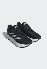 Scarpe sportive nere con tomaia in rete, righe bianche Adidas, colletto imbottito e suola spessa bianca. Il design è leggero e traspirante.