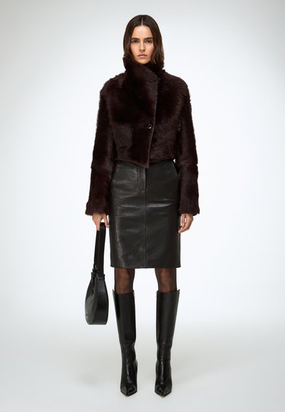 Giacca corta in pelliccia sintetica bordeaux con colletto ampio, abbinata a una gonna a tubino in pelle nera. Stivali neri al ginocchio con punta appuntita e borsa nera.