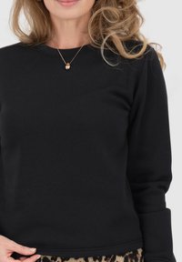 Felpa nera con maniche lunghe, scollo rotondo e orli a costine. Presenta una texture liscia ed è abbinata a una gonna con stampa. Accento con collana dorata.