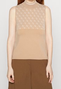 Top senza maniche beige con collo alto, caratterizzato da un design a maglia con motivo tonale nella parte superiore e una sezione inferiore liscia.