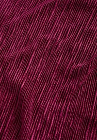 Texturovaná látka v hluboké burgundské barvě, se svislými žebry vytvářejícími vlnitý vzor, vyrobená z měkkého, lesklého materiálu s nádechem lesku.
