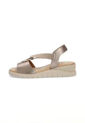 Sandalia con un upper de metalizado dorado, tira elástica y una suela de cuña beige baja y texturizada. Presenta un diseño entrecruzado y una punta redonda.