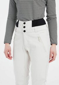Witte skibroek met een hoge tailleband, drie zwarte knopen, zijzakken met rits en een gladde textuur, gecombineerd met een zwart-wit geblokte top.
