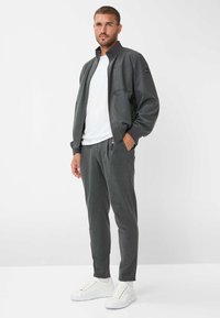Grijze zip-up jas met een hoge kraag, twee voorkezen; gecombineerd met bijpassende grijze broek en witte sneakers. Gladde textuur.