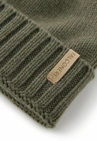 Stickad mössa i mörkgrön ull, med ribbat mönster och en tanfärgad läderetikett präglad med "FALCONIER".