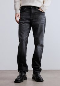 Fekete, egyenes szabású farmernadrág finom fakulással, öt zsebbel, övbújtatókkal és klasszikus gombsorral.