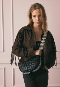 Fekete steppelt táska fehér csillagmintás pánttal, átlósan viselve, barna leopárdmintás rojtos dzseki és fekete felső társaságában.