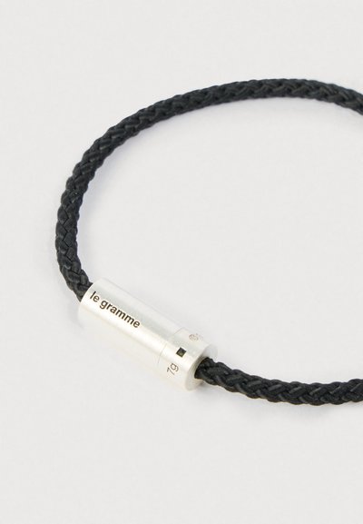 Pulseira de cordão trançado preto com fecho cilíndrico em prata gravado com "le gramme" e "7g" sobre um fundo branco.
