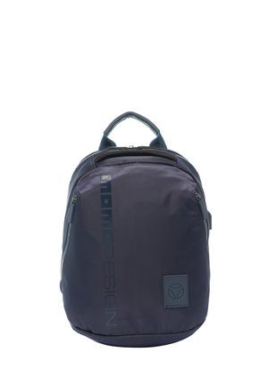 Sac à dos compact bleu foncé avec poignée supérieure, poches zippées frontales, nom de marque vertical, et petite étiquette carrée avec logo en bas à droite.