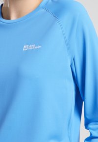 Lichtblauw langemouwen shirt van gladde stof, met een ronde halslijn, raglanmouwen en een wit logo op de borst.