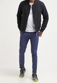 Dark navy bomber jacket, white t-shirt, slim-fit blue pants, and gray sneakers with green accents. Simple design, casual look.