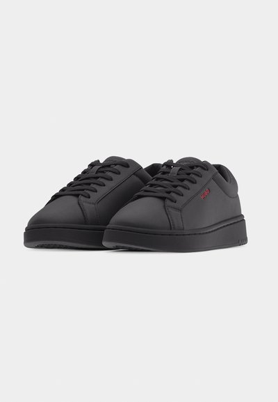 Paire de baskets noires basses à lacets avec semelles épaisses et marquage rouge "HUGO" sur le côté, présentées sur un fond clair uni.