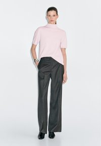 Maglione corto rosa a maglia con collo alto abbinato a pantaloni larghi scuri e scarpe nere semplici. Tessuto liscio, fit moderno.
