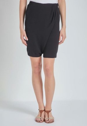 Pantalones cortos de tela negra con un diseño drapeado, cintura elástica y una textura suave. Combinados con sandalias marrones que muestran tiras finas.