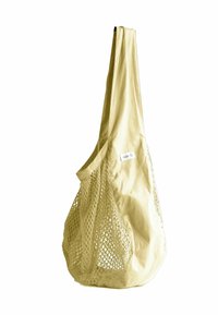 Beżowa, wielokrotnego użytku torba na zakupy z bawełny siatkowej z szerokim paskiem i małą etykietą z organicznego materiału po boku.